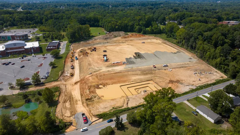 Aerial view of a graded site with crews placing stone base
