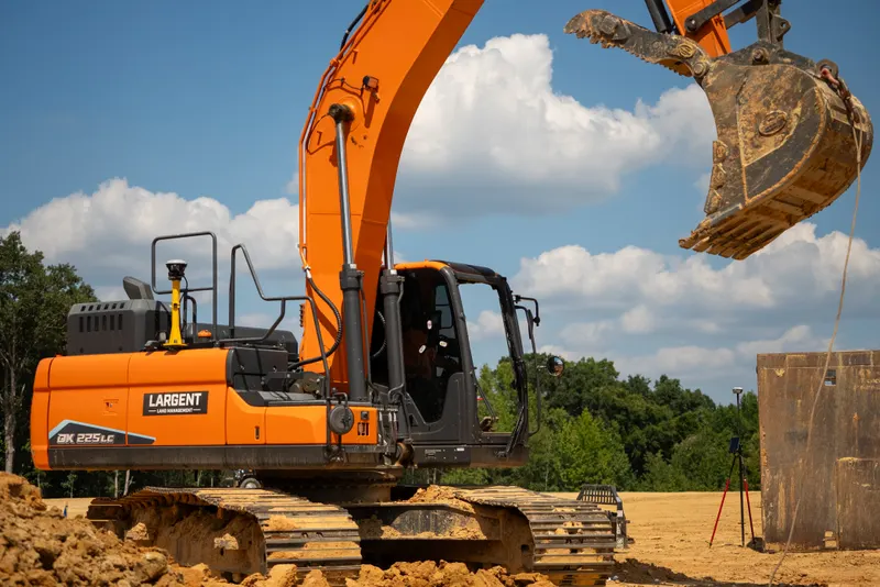 Largent excavator with its bucket raised beside a trench box