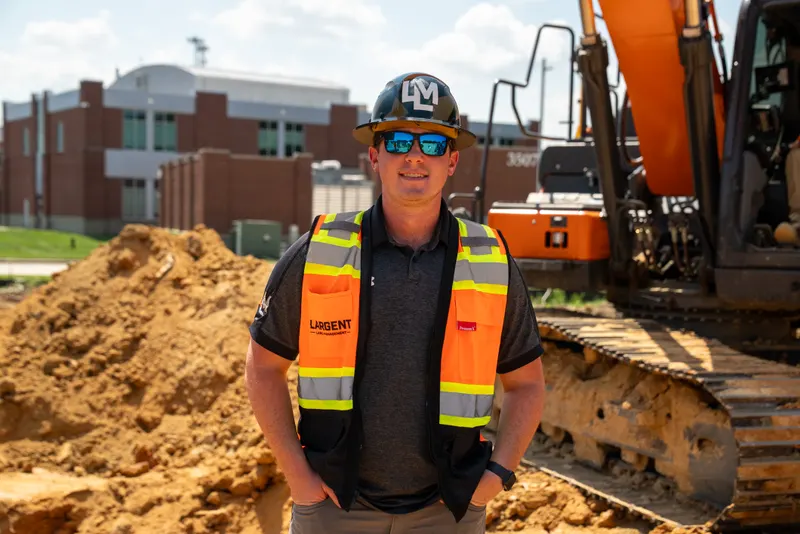 Largent site lead in an LM hard hat and safety vest beside an excavator