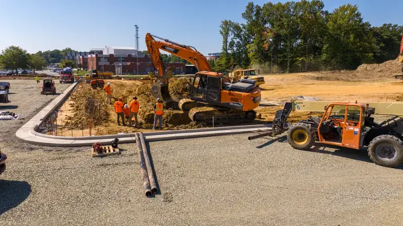 Excavator digging the water line trench beside new curb, crew and telehandler on site