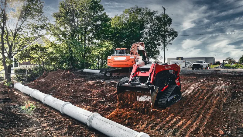 Skid steer placing storm pipe on a graded site